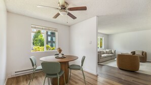 A modern living room with a dining area, a ceiling fan, hardwood flooring, and a view of a cityscape through large windows. - Comfortable Townhouse in Ash Way Lynnwood (Lynnwood)