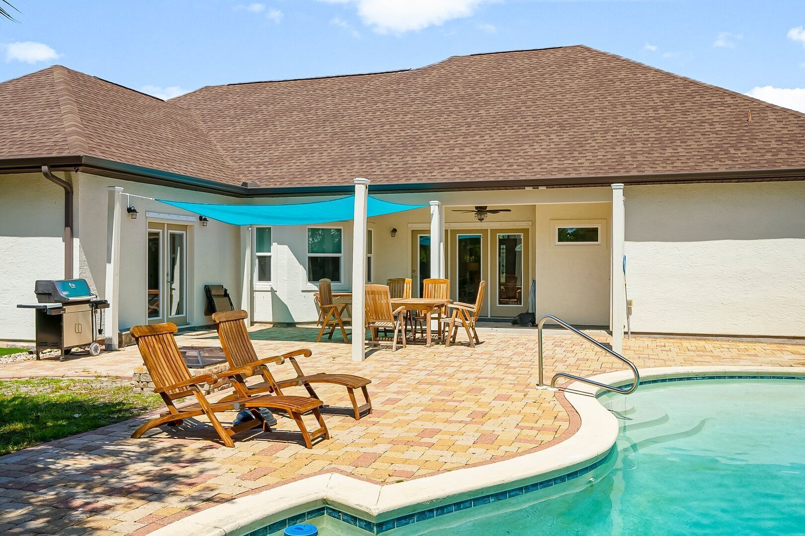 Ein Poolbereich mit überdachter Terrasse, Gartenmöbeln und Grill.