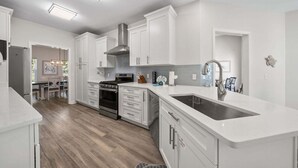 A modern kitchen with white cabinetry, a stainless steel stove, and a large sink.