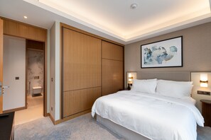 A hotel room with a large bed, wooden wardrobe, and a painting on the wall.