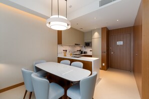 A modern kitchen with a white countertop, a microwave, and a sink. There is a dining area with a white table and blue chairs. - Address Dubai Opera 2BR | Walk to Mall, Burj Khalifa & Opera (Dubai)
