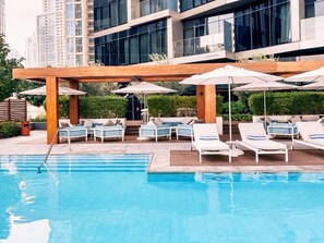 A swimming pool with lounge chairs and umbrellas, surrounded by a wooden pergola.