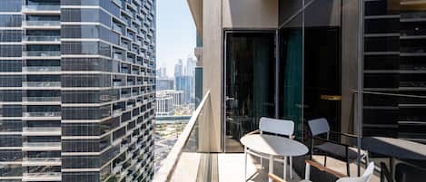 Un bâtiment moderne doté d’un balcon en verre, de chaises blanches et d’une table.