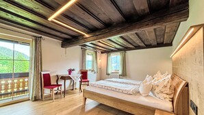 A bedroom with a wooden ceiling, a bed with floral bedding, a wooden desk, and a chair.