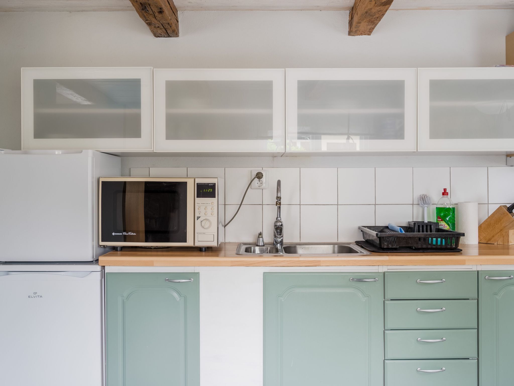 A kitchen with white cabinets, a microwave, a sink, and a green refrigerator.