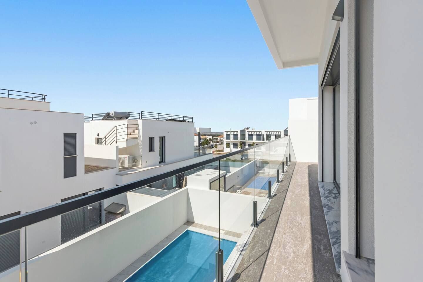 Um edifício moderno com piscina no terraço, guarda-corpos de vidro e vista ampla da região.