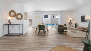 A modern living room with a dining area, a pool view, and a TV.