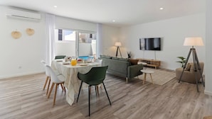 A modern living room with a dining area, a sofa, a TV, and a lamp.