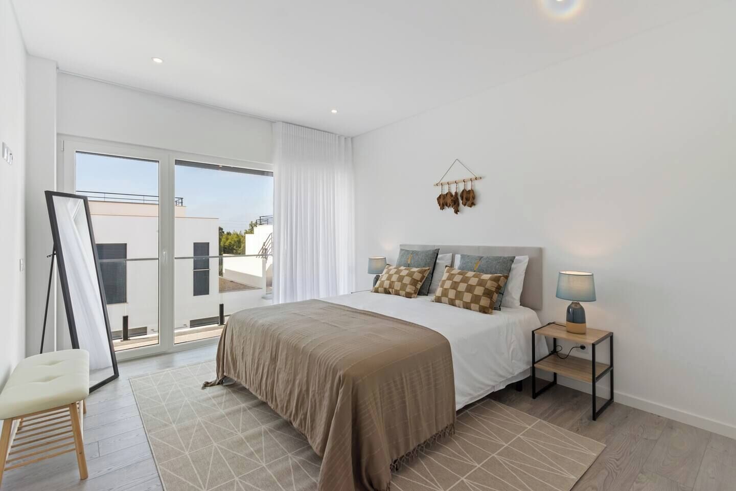 Quarto moderno com uma cama grande, uma mesa de cabeceira com abajur e vista para o exterior por uma porta de correr.