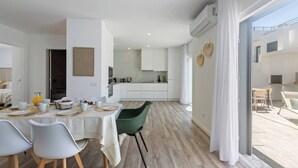 A modern kitchen with white cabinets, a dining area with a table set for four, and a large sliding glass door leading to an outdoor seating area.