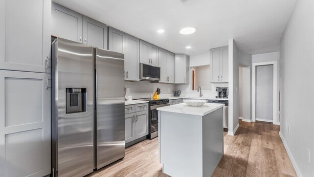 A modern kitchen with stainless steel appliances, grey cabinetry, and a central island. - Dockside Delight! Waterfront Home + Boat Slip for Your Next Getaway (New Port Richey)