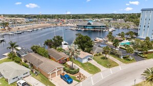 A marina with boats docked, a large building with a blue roof, and residential houses with lawns and palm trees. - Dockside Delight! Waterfront Home + Boat Slip for Your Next Getaway (New Port Richey)