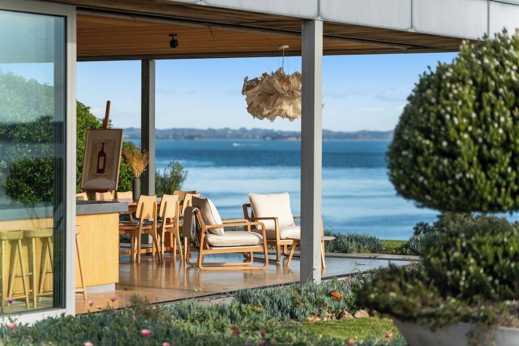 A modern outdoor seating area with a view of the sea, wooden furniture, and a hanging light fixture.