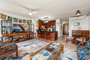 Una sala de estar con televisor, muebles de madera, una zona de cocina y un comedor.