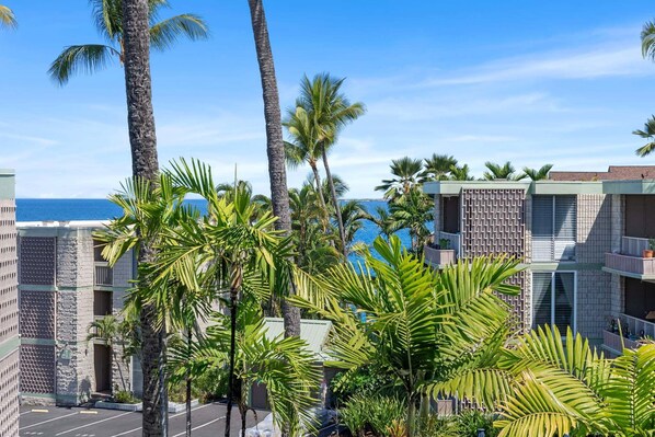 Un hotel con vista al océano, palmeras y un estacionamiento.