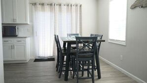 Een moderne keuken met witte kasten, een magnetron en een eethoek met tafel en stoelen.