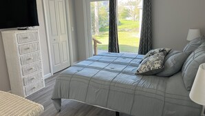 Een slaapkamer met een bed, een televisie, een kledingkast en een raam met gordijnen.