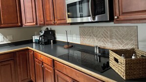 Una cocina con armarios de madera, microondas de acero inoxidable, cafetera y una cesta tejida.