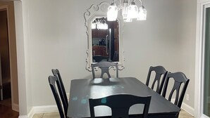 Un comedor con una mesa rectangular, seis sillas, una araña y un espejo grande.
