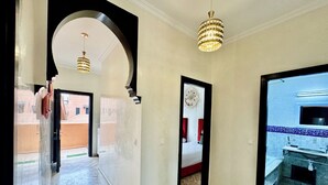 A hotel corridor with a marble floor, a chandelier, and a view of a bathroom with a tiled backsplash.