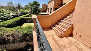 A building with a staircase leading to a second floor, surrounded by well-maintained gardens and a clear blue sky.