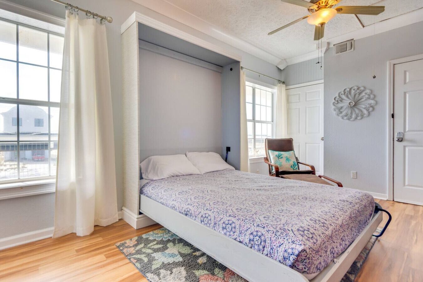 Une chambre avec un lit, une chaise, un ventilateur de plafond et une vue sur l’extérieur.