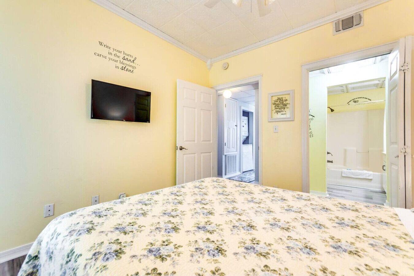 A bedroom with a floral bedspread, a mounted TV, and a door leading to a bathroom.
