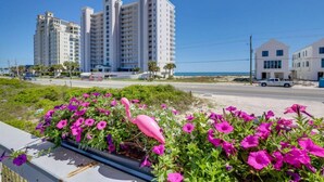 A coastal hotel with multiple high-rise buildings, a sandy beach, and a flower bed with pink flowers. - Deck + Gulf of America View: `Sunrise` on Perdido Key! (Pensacola)