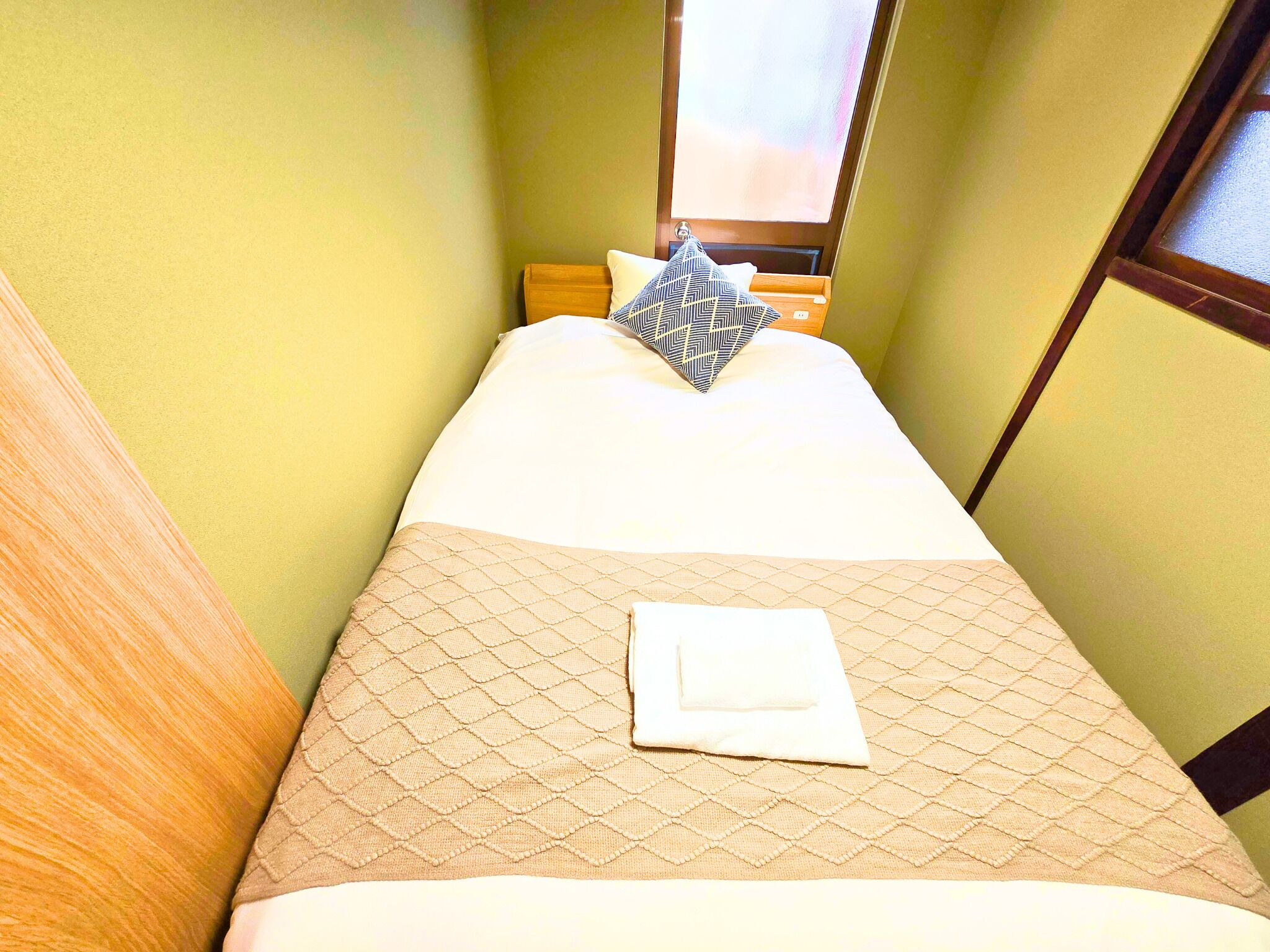 Habitación de hotel estrecha con cama, ventana y cabecera de madera.