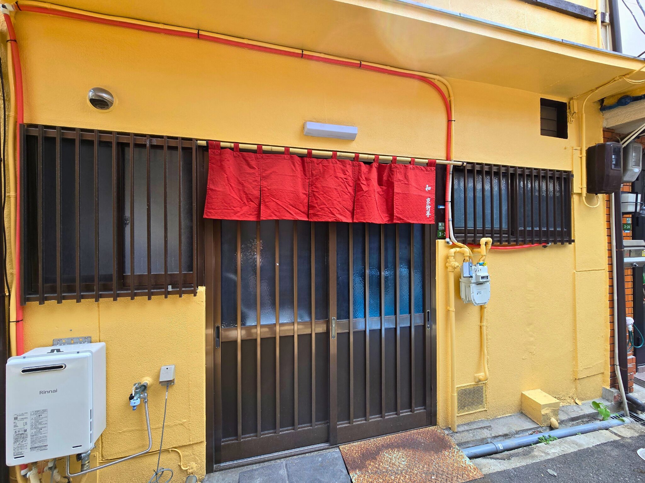 A yellow building with a black metal gate, a red awning, and a water heater on the wall.