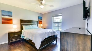 A bedroom with a bed, nightstands, a ceiling fan, a window, and a TV mounted on the wall.