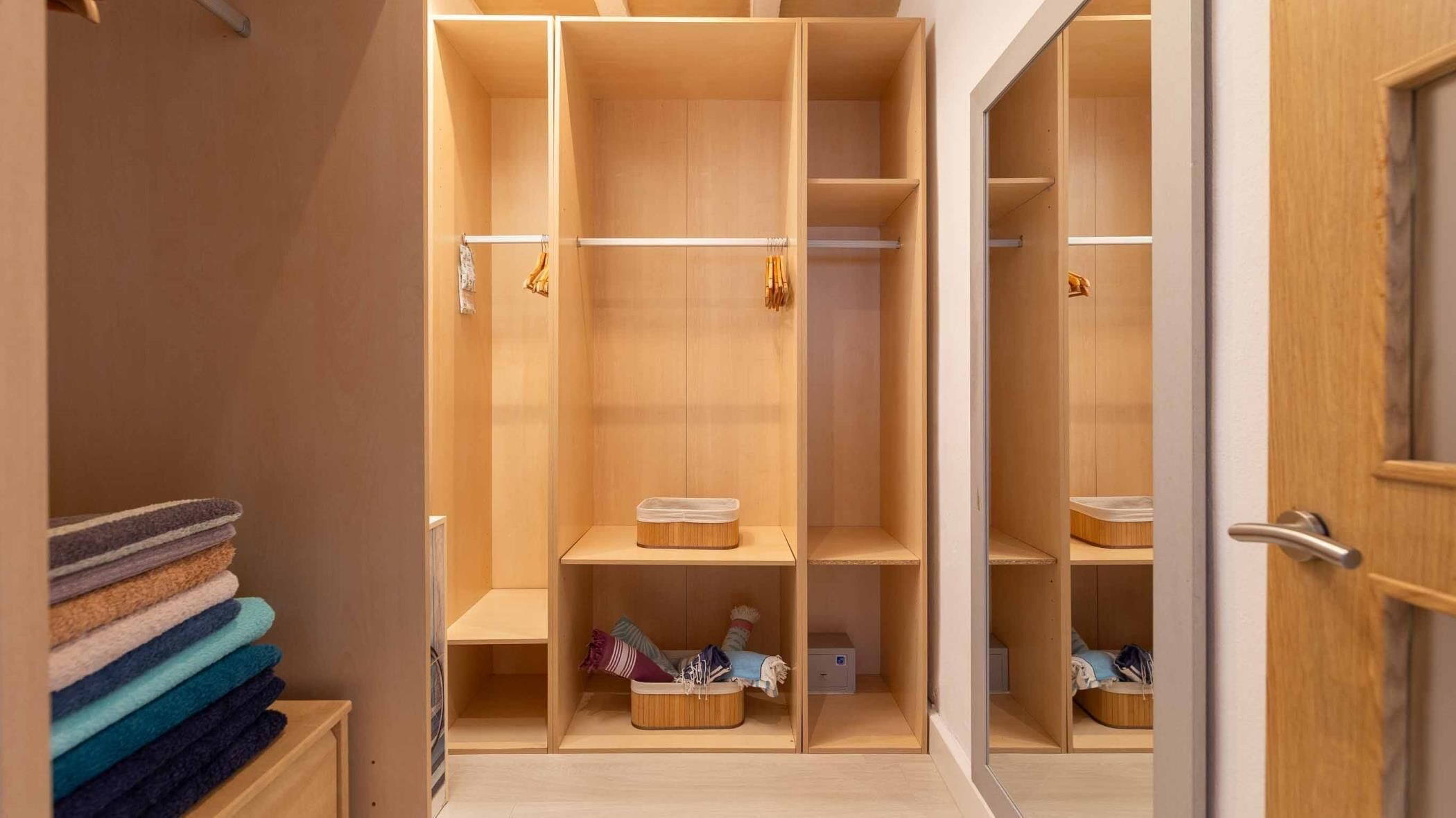 Un vestidor con amplios estantes de madera y espacio para colgar, un perchero metálico y una puerta con manija.