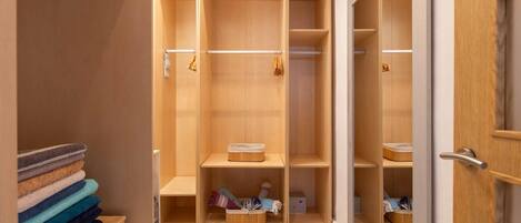 Un vestidor con amplios estantes de madera y espacio para colgar, un perchero metálico y una puerta con manija.