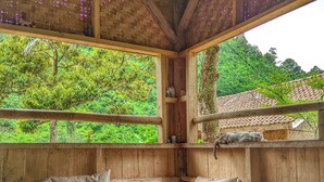 A cozy corner with a cushioned bench, a small table with a teapot, a basket of bananas, and a spiky fruit. - Farmstay Manangel (Cianjur)