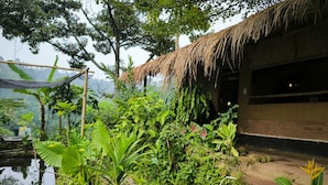 A rustic building with a thatched roof, surrounded by lush greenery and a pond. - Farmstay Manangel (Cianjur)