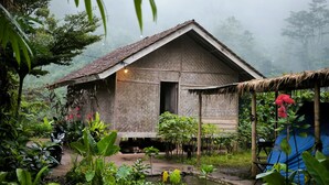 A rustic wooden house with a thatched roof, surrounded by lush greenery and a small pond. - Farmstay Manangel (Cianjur)
