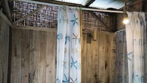 A rustic bathroom with wooden walls, a metal roof, and a window with a metal grill. - Farmstay Manangel (Cianjur)