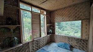 A room with a bed, a window with a view of greenery, and shelves with plants and books. - Farmstay Manangel (Cianjur)