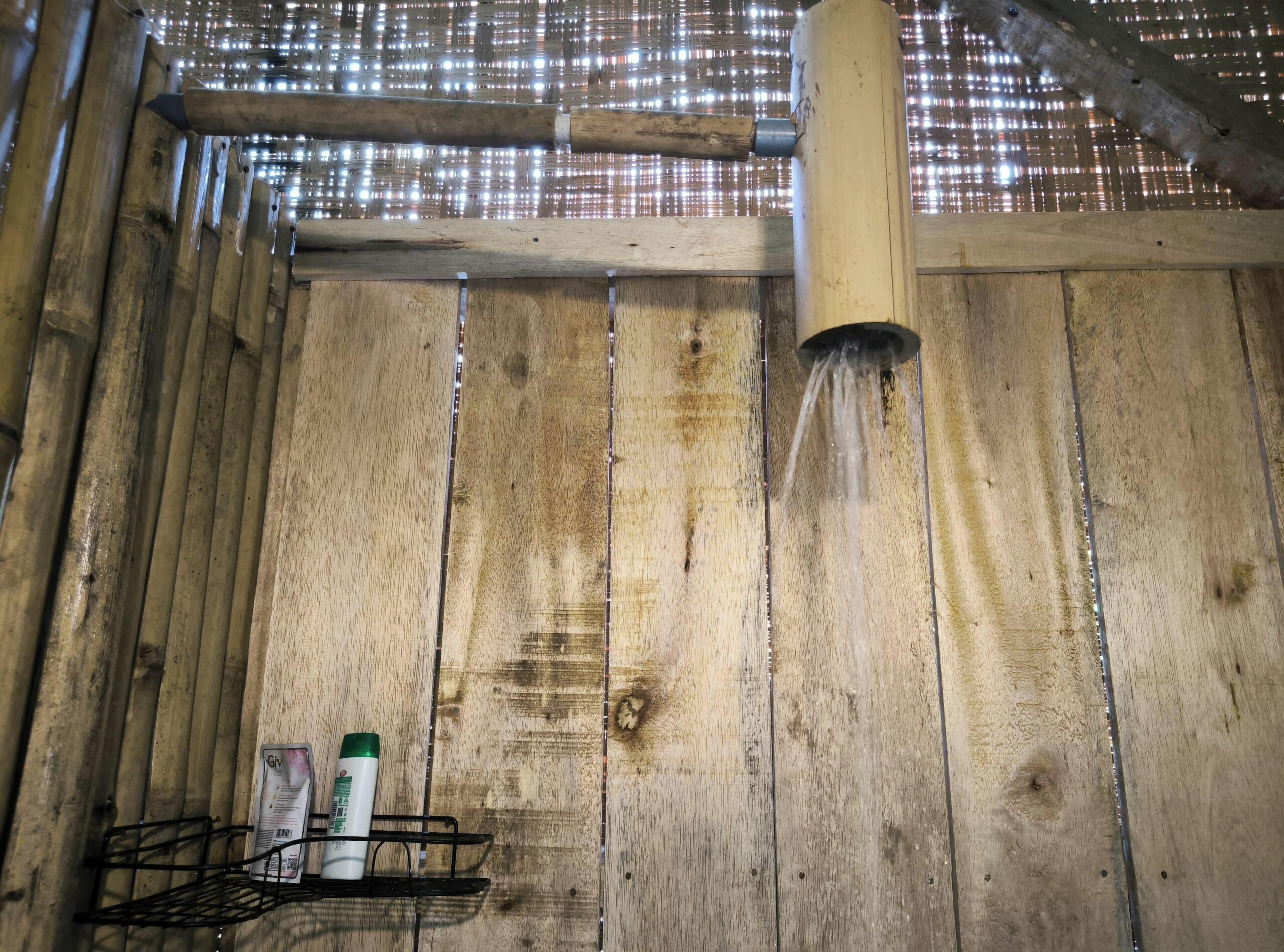 Et træpanelt interiør med et bruseområde, et metalstativ med toiletartikler og et loft med reflekterende materiale.