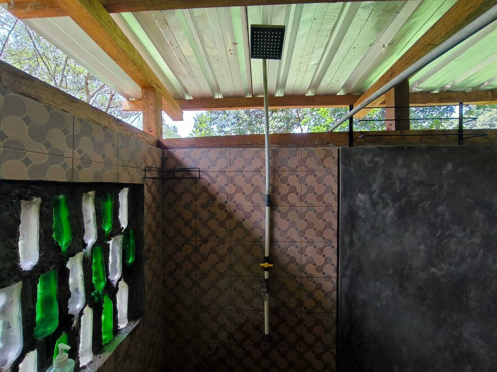 A shower area with a tiled wall, a green glass shower enclosure, and a ceiling with wooden beams.