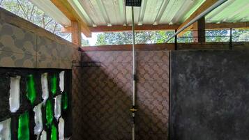 A shower area with a tiled wall, a green glass shower enclosure, and a ceiling with wooden beams.