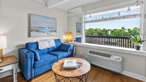 A living room with a blue sofa, a wooden coffee table, and a large window with a view of greenery.