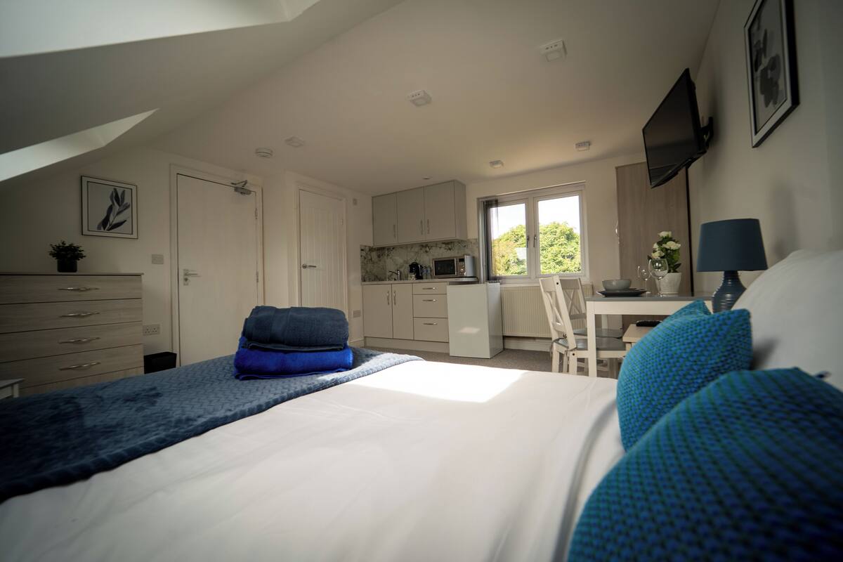 A bedroom with a bed, a desk, and a kitchenette.