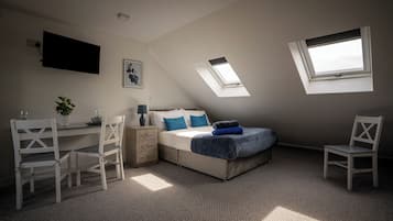 Un dormitorio con cama, escritorio, sillas, televisor y tragaluces.