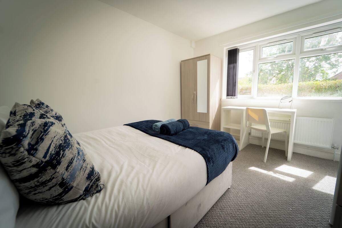 A bedroom with a bed, a desk, and a window.