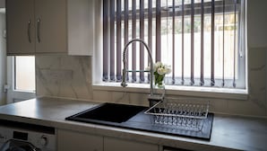 A kitchen with a modern design, featuring a built-in stove, a sink with a faucet, and a window with vertical blinds. - Beckbury House (Birmingham)