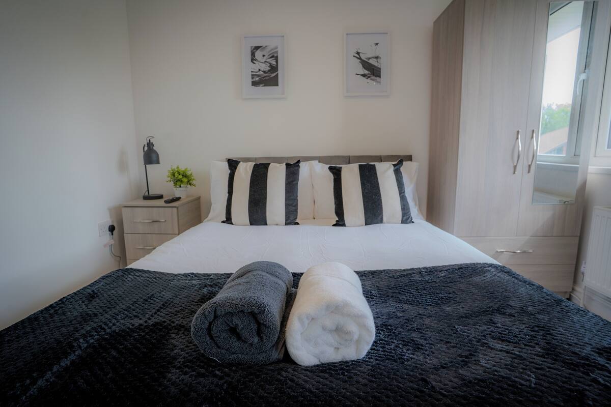 A neatly made bed with a black and white striped headboard, two pillows, and two rolled towels.