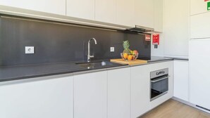 A modern kitchen with white cabinets, a stainless steel sink, a built-in oven, and a fruit bowl on the countertop.