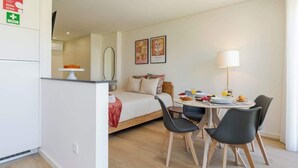 A compact hotel room with a bed, a dining area with a table and chairs, and a small kitchenette.