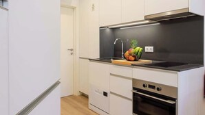 A modern kitchen with white cabinetry, a black countertop, a stainless steel range hood, and a built-in oven.